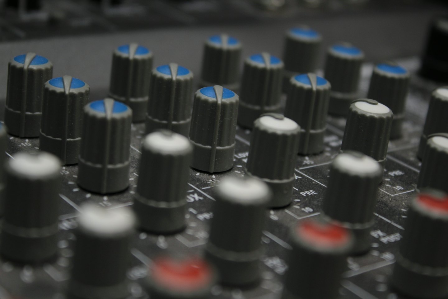 Audio mixing board with many grey knobs and colored indicators.